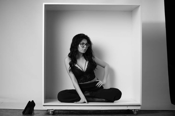 сексуальная красивая брюнетка женщина в нижнем белье и модные брюки колокольчика позирует в декоративной коробке в студии на белом фоне  - Фото, изображение