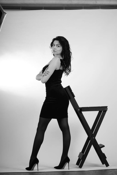 szexi gyönyörű barna nő kis fekete ruha és harisnya magas sarkú pózol stúdió fehér háttér  - Fotó, kép
