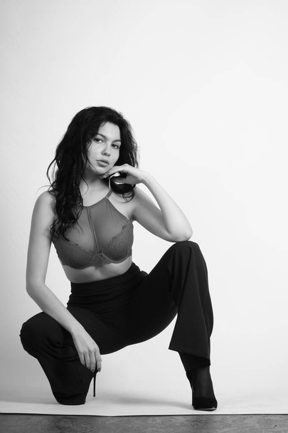 сексуальная красивая брюнетка женщина в нижнем белье и модные брюки колокольчика позирует в студии на белом фоне  - Фото, изображение