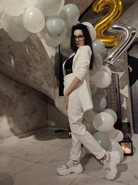 belle femme brune en costume blanc tendance posant avec des ballons d'anniversaire à la maison  - Photo, image