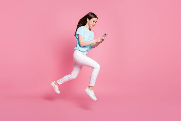 Full length profile side photo of girl jump use smartphone run wear t-shirt trousers isolated pastel color background - Fotoğraf, Görsel