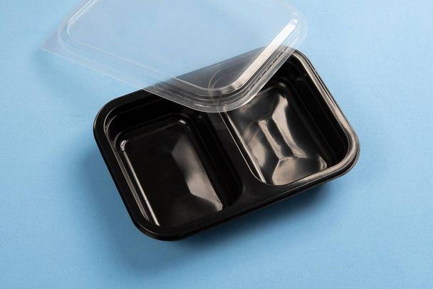 Contenedor de plástico negro para servicio de entrega de alimentos en un fondo azul - Foto, Imagen