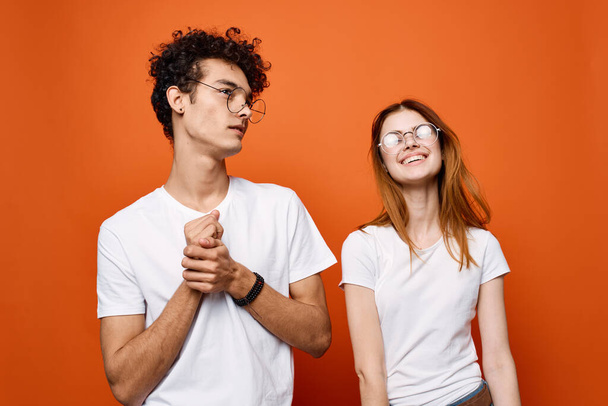 curly guy and a girl in white t-shirts are standing next to each other on an orange background - Фото, изображение
