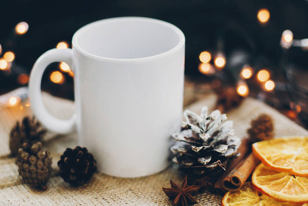 Beyaz boş bardak ve çam kozalağı, anason, tarçın, arkaplanda kurutulmuş portakallar. Sıcak kakao ve çay zamanı. Noel tatili - Fotoğraf, Görsel