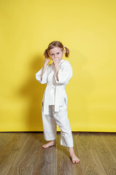 Portrait Of 5 year old caucasian Girl in kimono Practicing Karate Against yellow Background at home - Fotografie, Obrázek