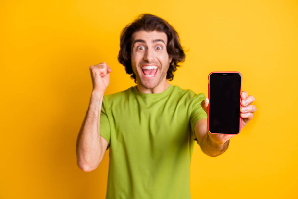 Portrait photo of amazed blurred man showing screen cellphone empty space gesturing like winner isolated on vivid yellow color background - Fotografie, Obrázek