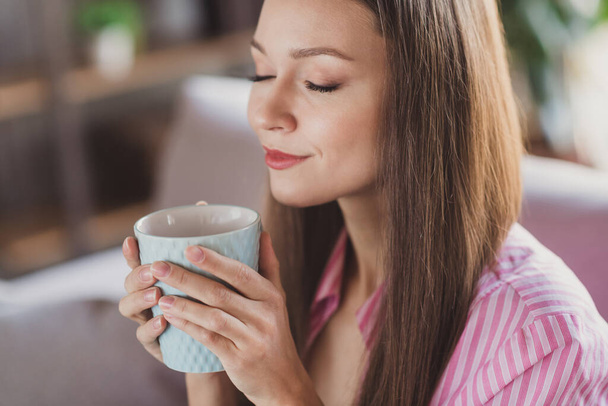 Photo of peaceful brown haired woman hold coffee mug smell aroma closed eyes inside house indoors home - Foto, imagen