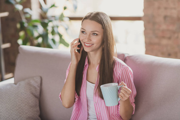 Photo of pretty sweet young woman dressed striped shirt sitting couch talking phone drinking tea inside indoors room - Foto, afbeelding