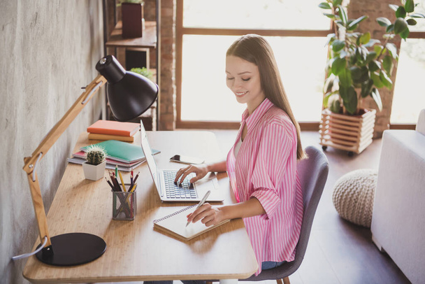 Profile side photo of brunette young woman sit desk write notebook laptop wear red striped shirt inside home indoors - Φωτογραφία, εικόνα