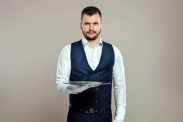 Handsome male waiter, in a white shirt, holds a silver tray on outstretched arms. The concept of serving staff serving customers in a restaurant - Photo, Image