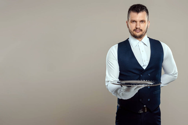 Handsome male waiter, white shirt, holds a silver tray, hand behind his back. Concept of wait staff serving customers in a restaurant - Foto, Bild