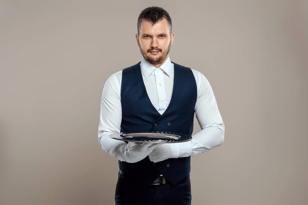 A male waiter in a white shirt and white gloves stands with a silver tray. The concept of service personnel serving customers in a restaurant - Photo, Image