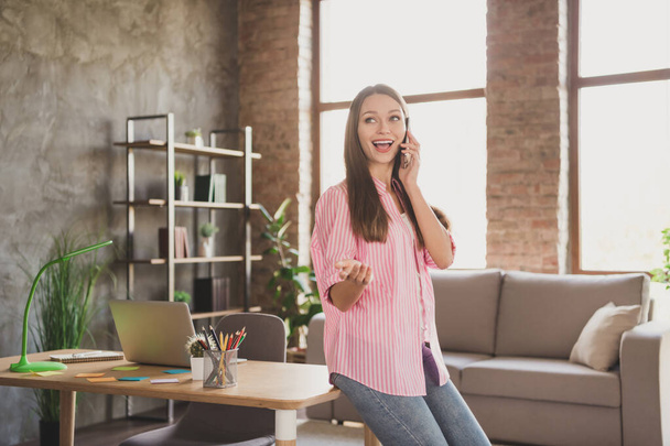 Profile photo of optimistic brunette lady talk telephone sit on table wear pink shirt jeans study from home - Foto, Imagen