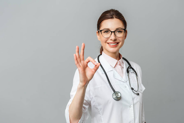 Portrait of a happy female doctor with a stethoscope showing the OK sign - Фото, изображение