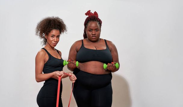 Picture of two afro women holding dumbbells and skipping rope, posing sexy - Foto, Bild