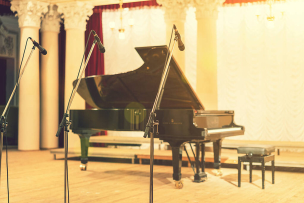 Μεγάλο πιάνο στο Μέγαρο Μουσικής. Πιάνο στέκεται σε άδεια σκηνή. άνοιξε μαύρο πιάνο με σκαμνί σε ξύλινη σκηνή συναυλιών. τονισμένο - Φωτογραφία, εικόνα