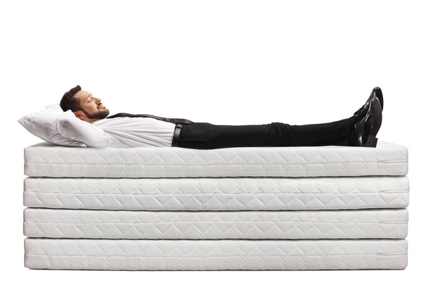 Businessman lying on a pile of mattresses with clothes and shoes isolated on white background - Foto, afbeelding