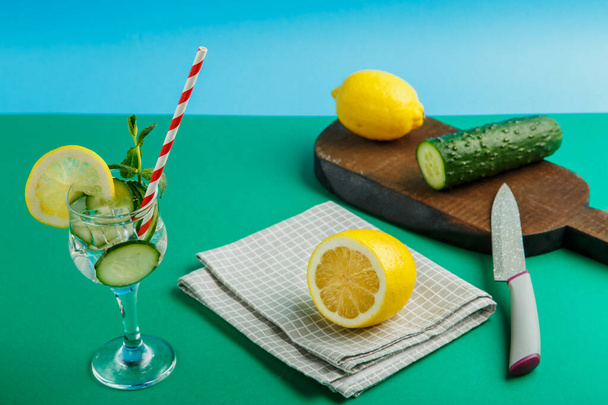 Cocktail cucumber water with lemon and mint in a glass on a napkin on a green background next to a lemon on a napkin. - Foto, imagen