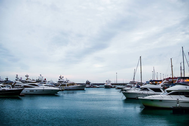 Luxury yachts docked in sea port at sunset. Marine parking of modern motor boats and blue water. Tranquility, relaxation and fashionable vacation. - Photo, Image
