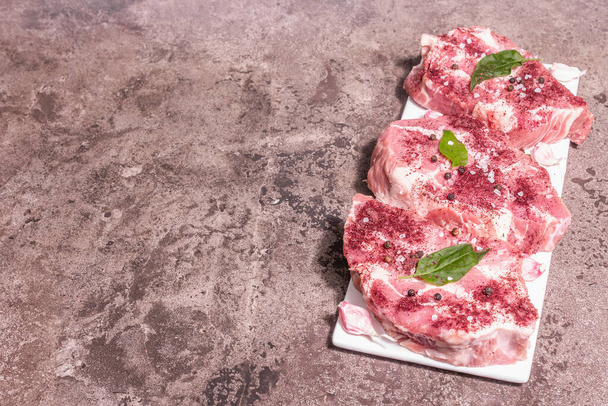 Raw pork meat, sliced cuts. Fresh meat, dry sumac, garlic and basil leaves. Healthy cooking food concept, trendy hard light, dark shadow. Marble stone background, top view - Foto, imagen