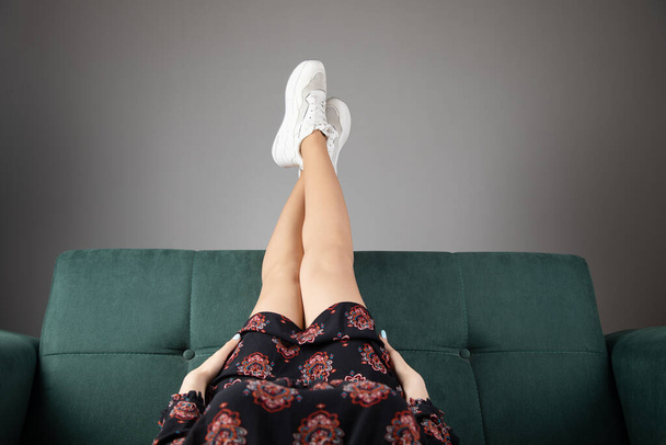 en casa en un sofá verde, las piernas de las mujeres se levantan alto - Foto, Imagen