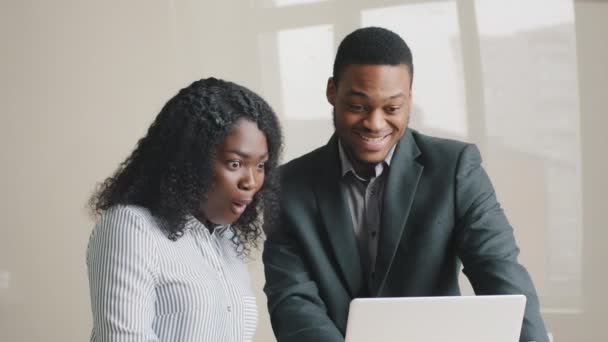 Aufgeregte junge multiethnische afroamerikanische Kollegen in offizieller Kleidung schauen glücklich auf den Laptop-Bildschirm, staunen, wenn sie E-Mails mit guten Nachrichten erhalten, feiern den Erhalt eines Traumjob-Angebots - Filmmaterial, Video