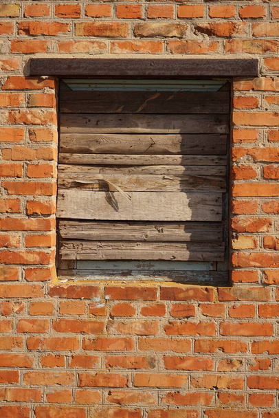 Fermé avec des planches de bois ouverture de fenêtre dans un vieux mur de briques rouges. - Photo, image