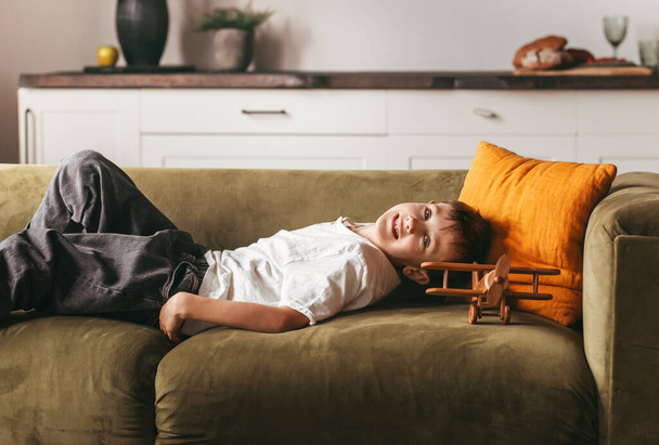 Egy fiú fekszik a kanapén egy játékgéppel és álmokkal. A gyermekek otthon töltött idejének koncepciója. - Fotó, kép