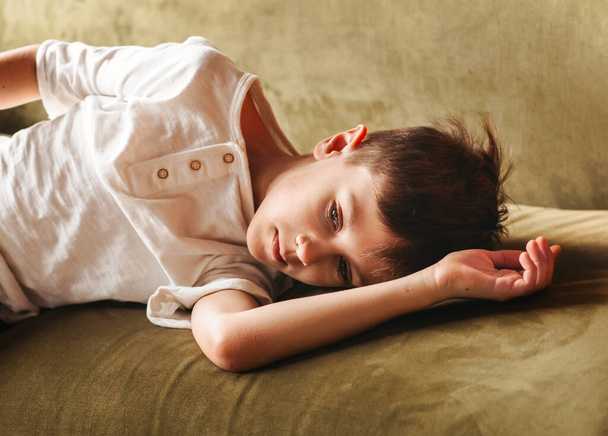 A sad boy lies on the sofa in the children's bedroom. Children's emotions. - Photo, Image