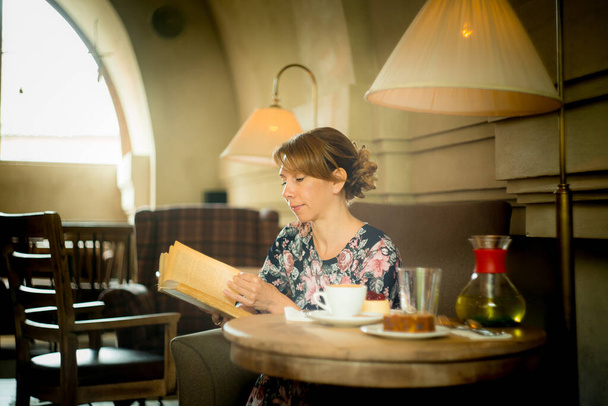 Красива жінка з книгою в руках. Жінка сидить у затишному кафе, читає і п'є каву
. - Фото, зображення