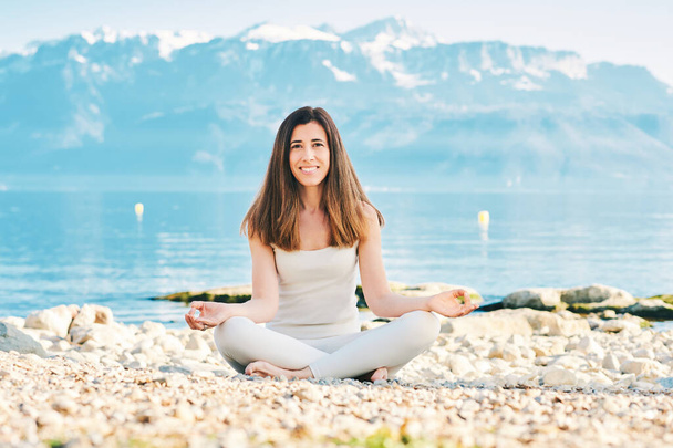 Piękna duchowa kobieta medytująca nad jeziorem, ubrana w beżowe ubrania - Zdjęcie, obraz