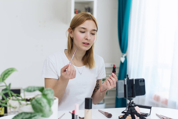 Beauty webinars, makeup classes online. Happy woman vlogger is showing cosmetics products while recording video stream on phone for her internet channel in social media. beauty blog about cosmetics - Foto, imagen