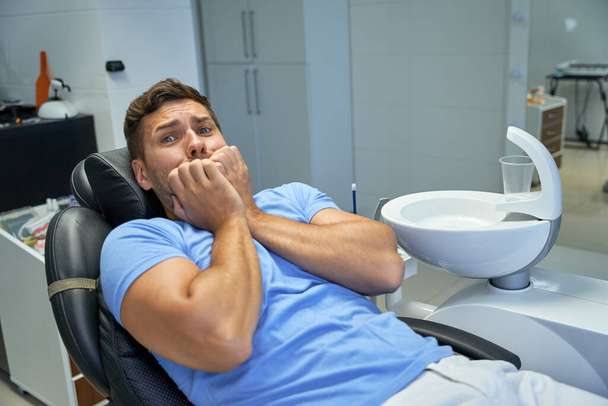 Φοβισμένος άντρας ασθενής που περιμένει οδοντιατρικό έλεγχο. - Φωτογραφία, εικόνα