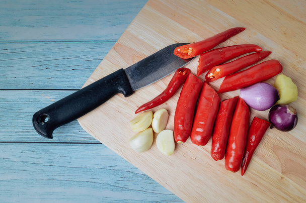 Pile of fresh red chillies, onions and garlic on wooden chopping board - Фото, зображення