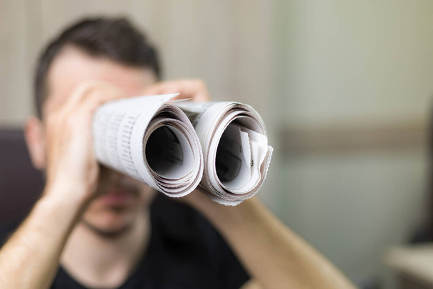 Man holding two twisted roll newspaper. Metaphor or allegory with binoculars. Selective focus on newspapers. Truth search concept - Foto, Imagem