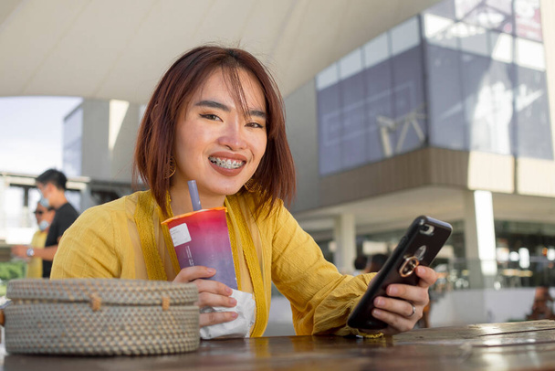 Eine moderne und modische asiatische Dame genießt eine kalte Tasse Milchtee in einem Einkaufszentrum im Freien oder auf dem Campus. - Foto, Bild