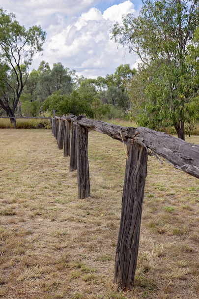 Старый деревянный забор реликвии ушедшей эпохи, стоящий в травянистом поле - Фото, изображение
