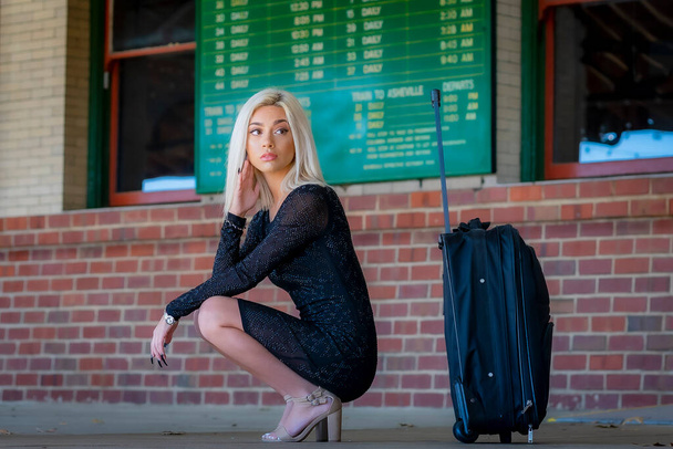Ένα πανέμορφο ξανθό μοντέλο ποζάρει στην ύπαιθρο περιμένοντας το τρένο σε μια αποθήκη τρένου. - Φωτογραφία, εικόνα
