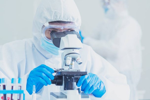Erkek bilim adamı bilim laboratuarındaki mikroskop araştırmalarına bakar. Asyalı bilim adamı laboratuvar kimya laboratuvarlarını arıyor. Covid-19 Coronavirus biyokimya araştırma deneyi aşı konsepti - Fotoğraf, Görsel