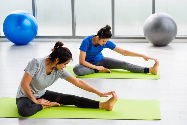 Two Asian women sporty attractive people practicing yoga lesson together, working out at the fitness GYM, Young and senior female exercising do yoga in yoga classes, sport healthy lifestyle - Foto, imagen