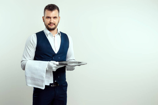 Hübscher männlicher Kellner in weißem Hemd, der ein silbernes Tablett in der Hand hält. Das Konzept der Bedienung von Mitarbeitern, die Kunden im Restaurant bedienen - Foto, Bild