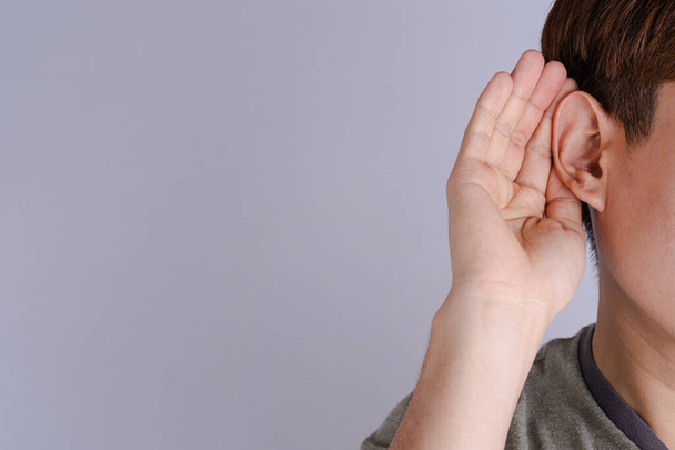pérdida auditiva del hombre o dificultad auditiva y tapar su mano detrás de su oreja aislar fondo gris, concepto sordo. - Foto, imagen