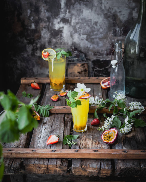 berry and passionfruit cocktails in glasses on wooden table with seasonal flowers and fresh fruit, refreshing drink concept - Foto, Imagem