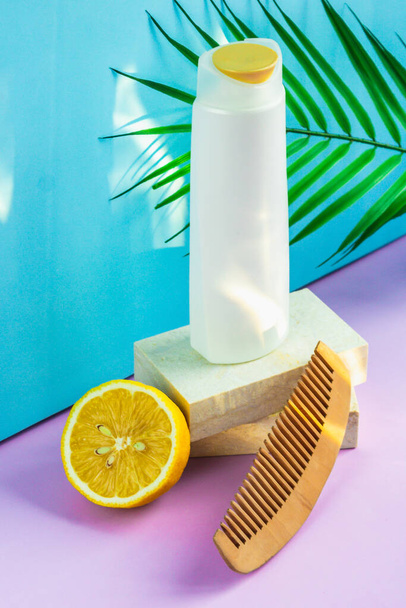 Hair cosmetics on a blue-purple background. an organic moisturizing shampoo sits on a granite slab podium, a comb with wide teeth for styling, and half a yellow lemon lies next to it. - Fotografie, Obrázek