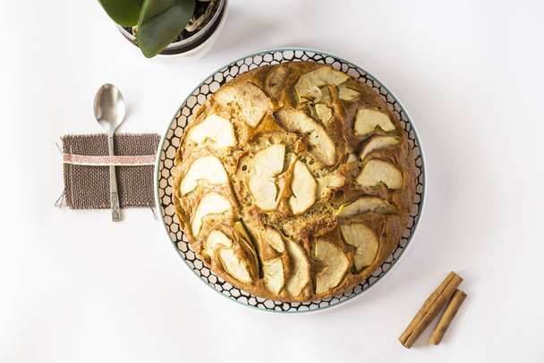 A top view of a delicious apple pie on a plate on a white surface with cinnamon sticks and a spoon on it - Foto, immagini