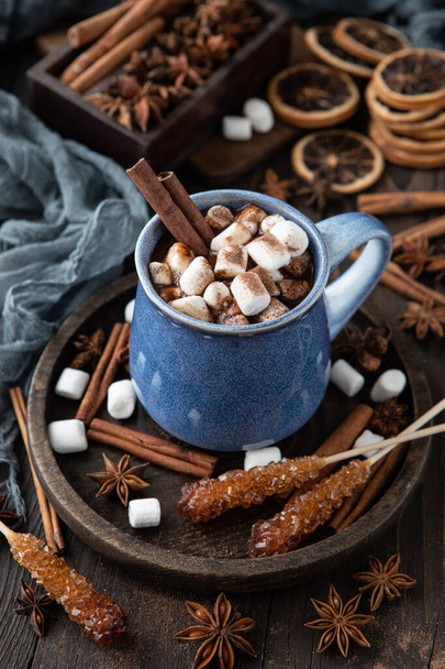 Hot chocolate with cinnamon sticks, anise,  marshmallows and cocoa powder on rustic wooden background, selective focus - Foto, Bild