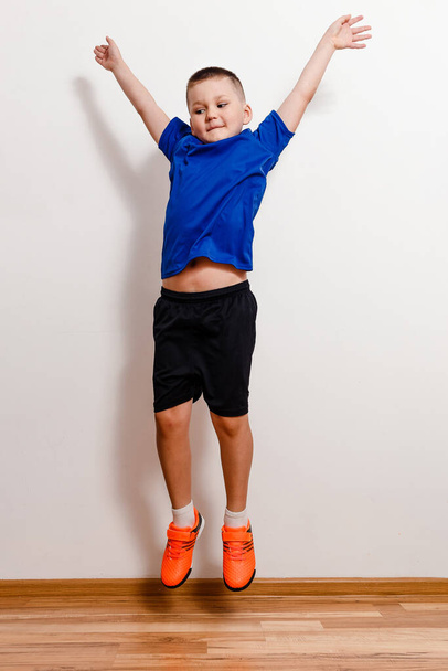 Seven-year-old boy in T-shirt and shorts jumps in sneakers on white background - Фото, изображение