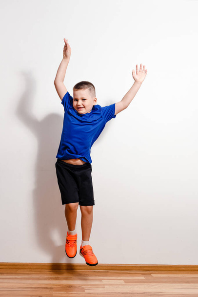 A seven-year-old short-haired boy jumps in sneakers against a white background. Children and sport - Zdjęcie, obraz