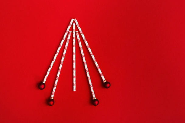 Creative christmas tree from drinking straws and New Year balls on red background. Holiday winter concept with bright colors. Minimal flat lay. - Фото, зображення