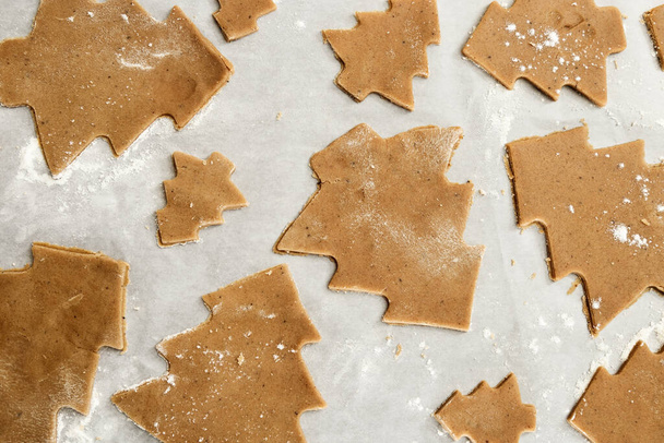 Gingerbread Cookie. New Year figures from a dough, prepared for baking in the oven. Biscuits in the form of a Christmas tree on paper for baking. Raw biscuit cookies. - Zdjęcie, obraz